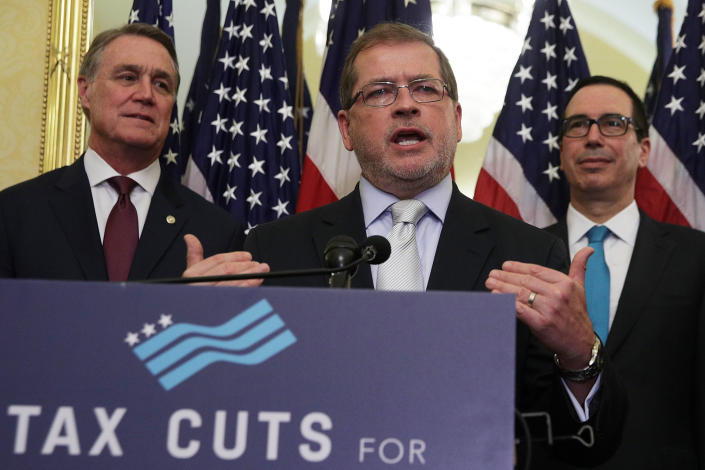Grover Norquist, flanked by Sen. David Perdue and Steven Mnuchin, at a podium marked with a sign saying: Tac Cuxts.
