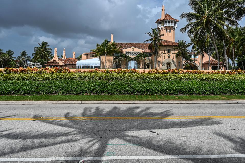 A view from the road of the buildings of Mar-a-Lago, amid palm trees.