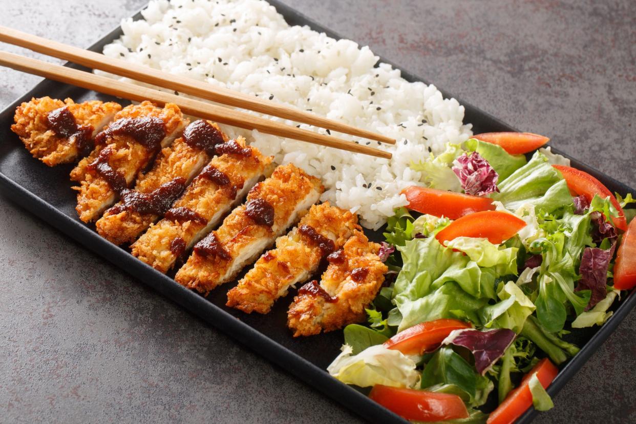 Chicken katsu is a Japanese dish that is also known as panko chicken or tori katsu served with rice and vegetables salad on the concrete table. Horizontal