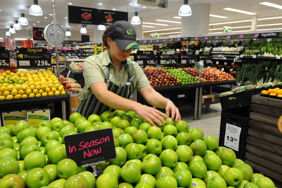 An employee arranges apples in the fruit and vegetable inside a Woolworths grocery store in Brisbane.