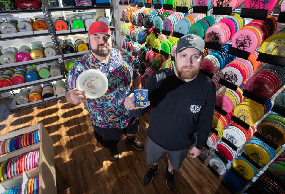 Emerald Coast Disc Golf Club officers Ryan Vann, right, holds a bag tag while Michael Osley holds a disc from the 2023 Gold Rush tournament at Flight Factory Discs in Pensacola on Monday, Dec. 18, 2023. ECDGC is preparing for the 2024 tournament that will be held in January.