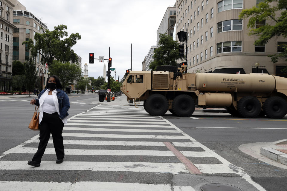 A woman walks across K Street as a military fuel truck passes by as demonstrators continue to protest the death of George Floyd, Tuesday, June 2, 2020, near the White House in Washington. Floyd died after being restrained by Minneapolis police officers. (AP Photo/Jacquelyn Martin)