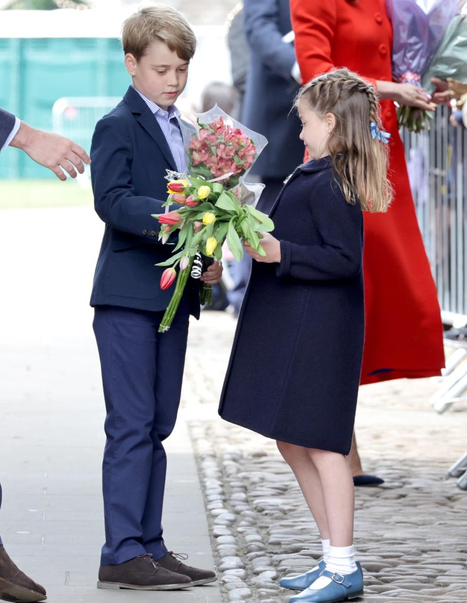 Prince George of Cambridge and Princess Charlotte of Cambridge hold gifts of flowers during a visit to Cardiff Castle