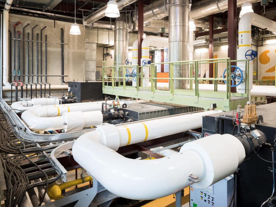 white tubing beneath a green metal bridge in a concrete room underground