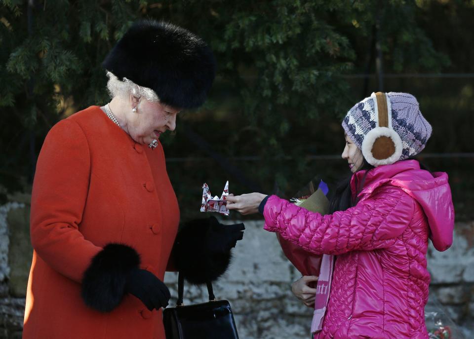 Britain's Queen Elizabeth II (L) receives gifts from children following a traditional Christmas Day Church Service at Sandringham in eastern England, on December 25, 2013. AFP PHOTO / ADRIAN DENNIS (Photo by Adrian DENNIS / AFP) (Photo by ADRIAN DENNIS/AFP via Getty Images)