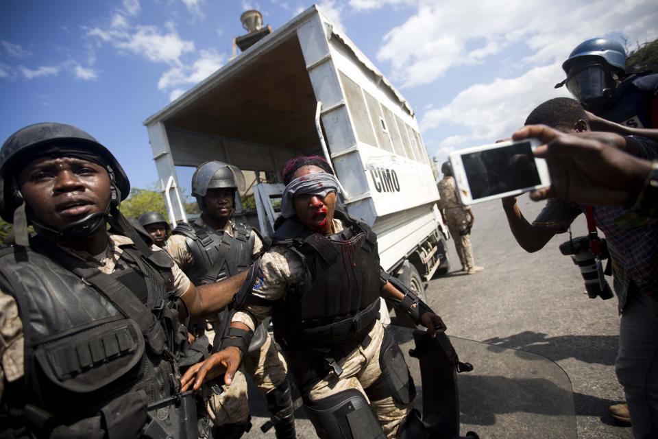 A national police officer is helped by fellow officers after she was hit in the face with a rock thrown by protesters demanding the resignation of Haitian President Jovenel Moise near the presidential palace in Port-au-Prince, Haiti, Wednesday, Feb. 13, 2019. Protesters are angry about skyrocketing inflation and the government's failure to prosecute embezzlement from a multi-billion Venezuelan program that sent discounted oil to Haiti. (AP Photo/Dieu Nalio Chery)