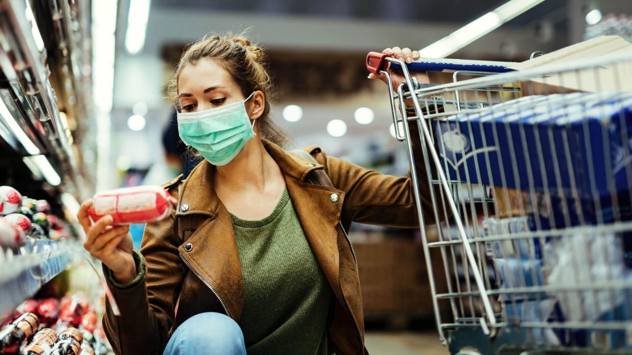 Young woman wearing protective mask and buying food in grocery store during coronavirus pandemic.