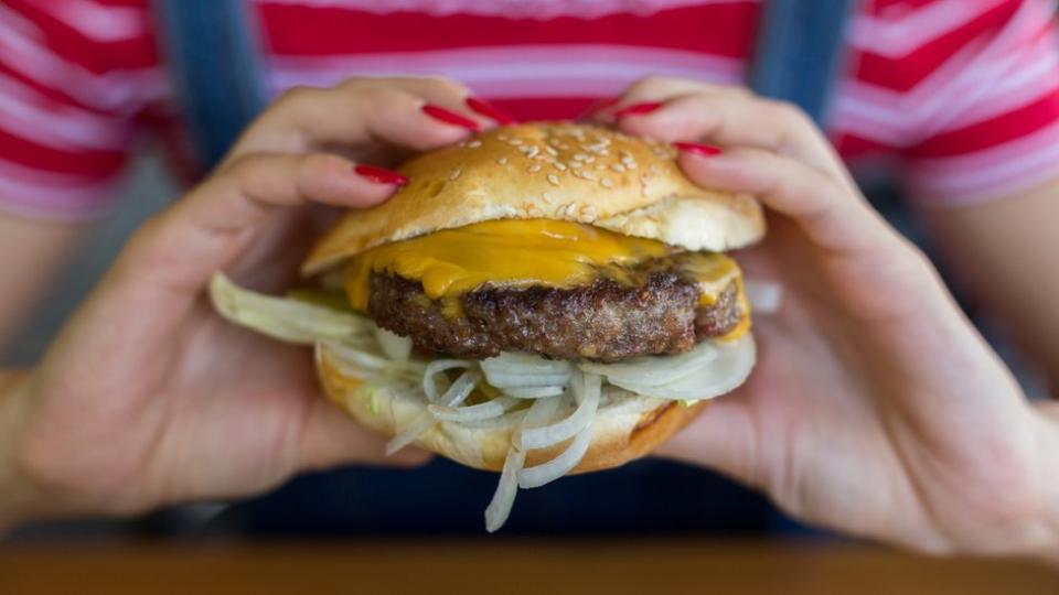 Manos sosteniendo una hamburguesa.