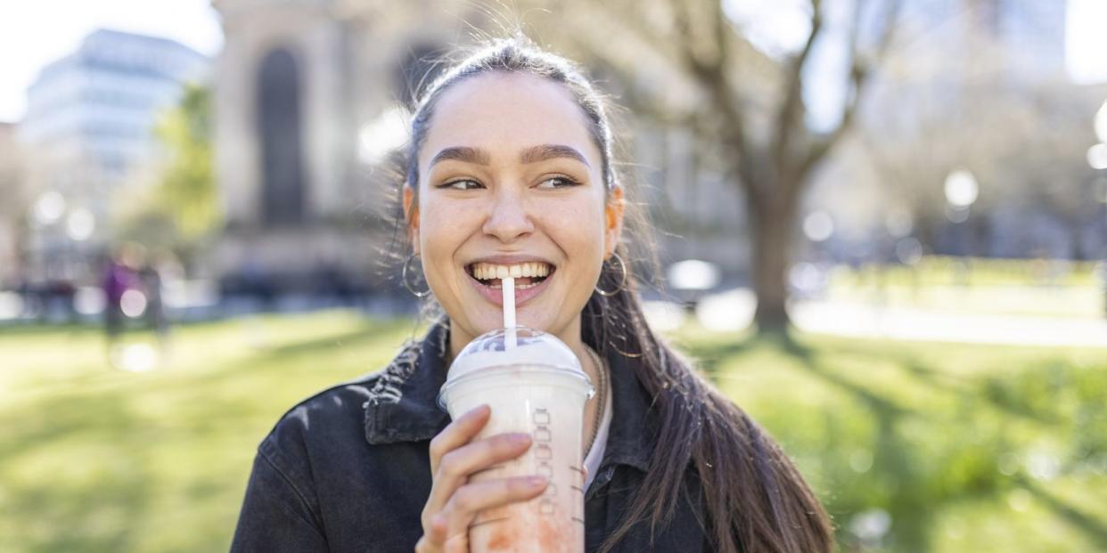 a woman drinking a smoothie in a park