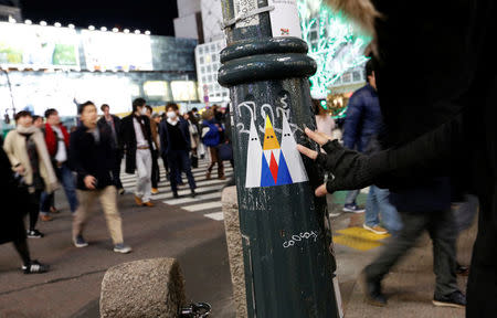 A Japanese graffiti artist known as 281 Antinuke fixes his sticker art depicting U.S. President Donald Trump, on a lamp post in Tokyo's Shibuya shopping and entertainment district, Japan, January 27, 2017. Picture taken January 27, 2017. REUTERS/Toru Hanai