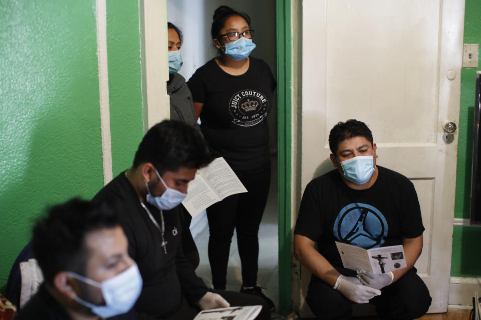 Family members wear personal protective equipment as the Rev. Fabian Arias performs an in-home service beside the remains of Raul Luis Lopez who died from COVID-19 the previous month, Saturday, May 9, 2020, in the Corona neighborhood of the Queens borough of New York. (AP Photo/John Minchillo)