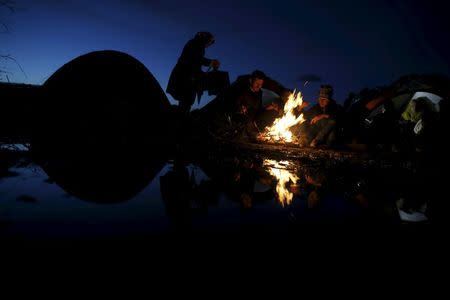 Migrants who are waiting to cross the Greek-Macedonian stand by the fire at a makeshift camp, near the village of Idomeni, Greece, March 4, 2016. REUTERS/Marko Djurica