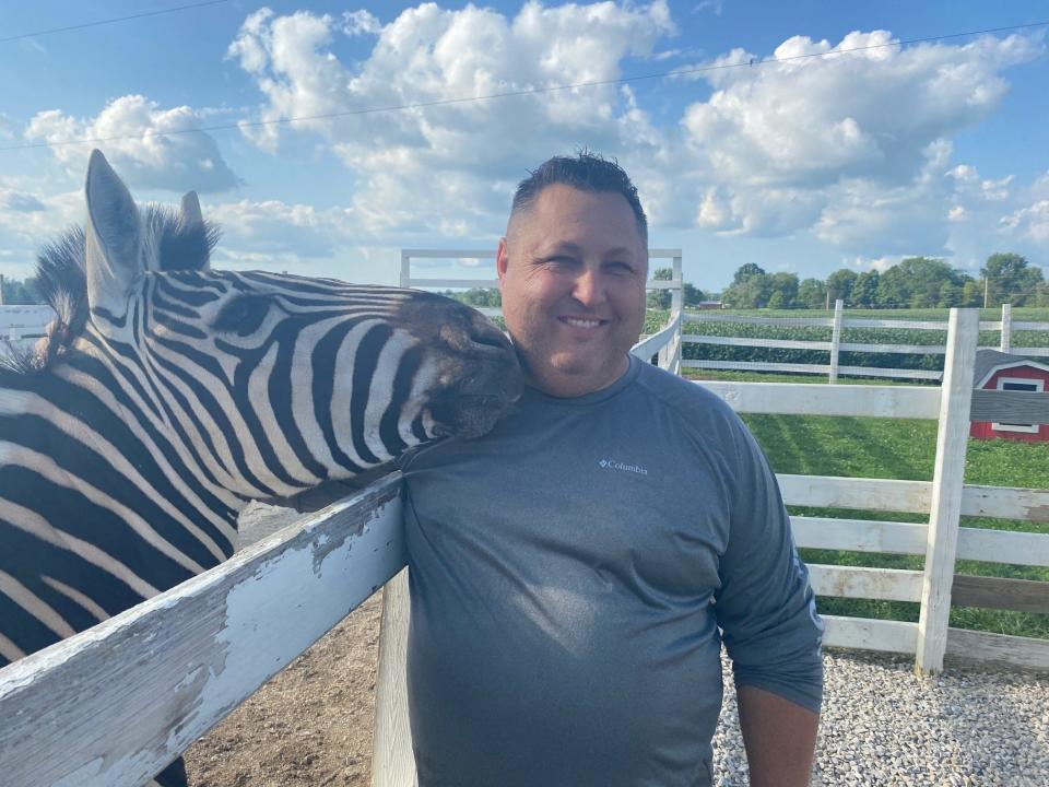 Shawn Westmeister gets a hug from Lincoln the zebra at his farm. The zebra is one of numerous animals on the farm owned by Shawn  and his wife Lynn at 4097 Plymouth-Springmill Road. Private tours are available for booking at Westmeister.com