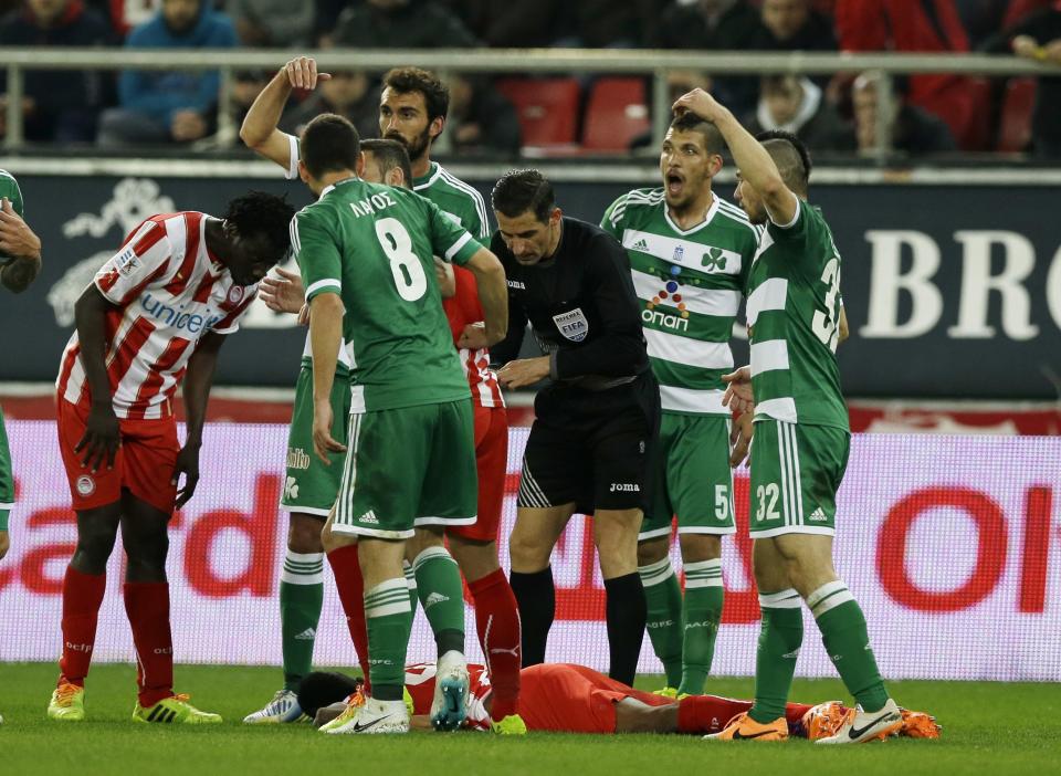 Olympiakos' Michael Olaitan of Nigeria lays on the pitch as Panathinaikos' players call for a medic during a Greek League soccer match at Georgios Karaiskakis stadium, in Piraeus port, near Athens, on Sunday, March 2, 2014. Olaitan collapsed suddenly when walking alone on the field and hit his head upon falling. He was carried away,on a stretcher and taken to a hospital for tests. (AP Photo/Thanassis Stavrakis)