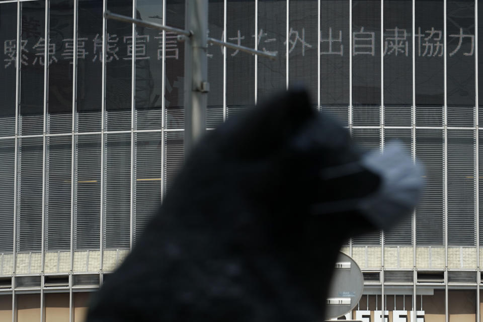 An electronic news bulletin board shows the message of cooperation of self-restraint following state of emergency, near a statue of a Japanese Akita dog named "Hachiko" wearing a face mask near Shibuya Station Wednesday, April 8, 2020, in Tokyo. Japanese Prime Minister Shinzo Abe declared a state of emergency yesterday for Tokyo and six other prefectures to ramp up defenses against the spread of the new coronavirus. Hachiko has waited for his owner University of Tokyo Prof. Eizaburo Ueno at the same place by the station every afternoon, expecting him to return home for nearly 11 years even after Ueno's death at work. (AP Photo/Eugene Hoshiko)