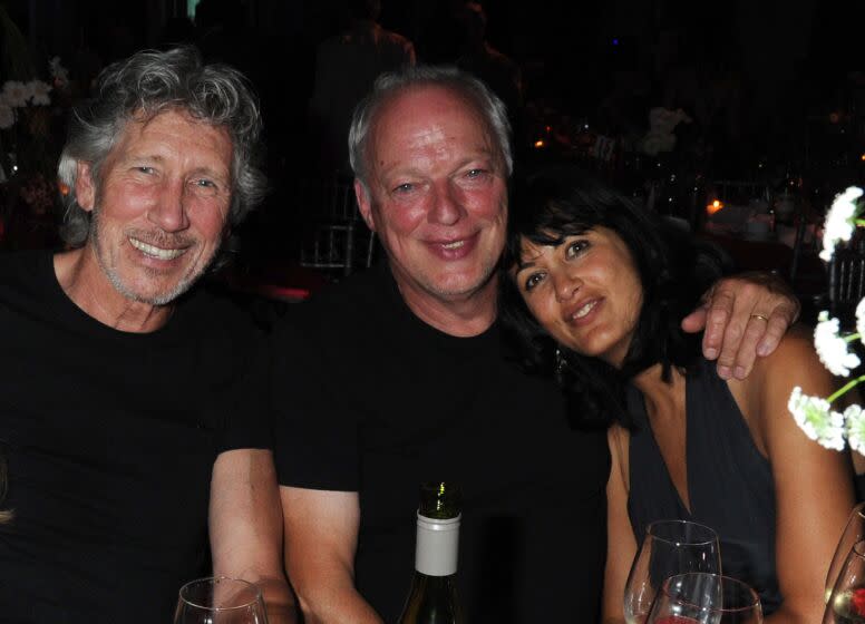 Two men and a woman sit at a table at an event. The man in the middle has his arm around the woman's shoulder.