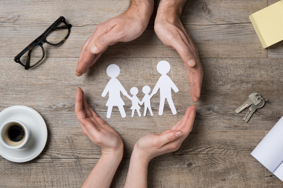 Two pairs of hands encircling a paper cut-out of a family.