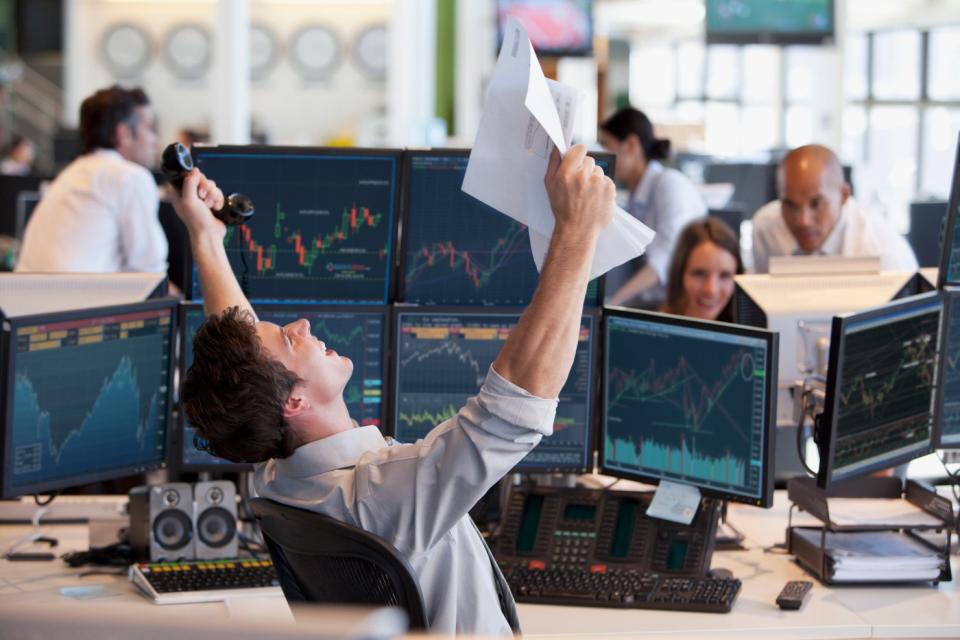 An investor celebrates while looking at several trading screens.