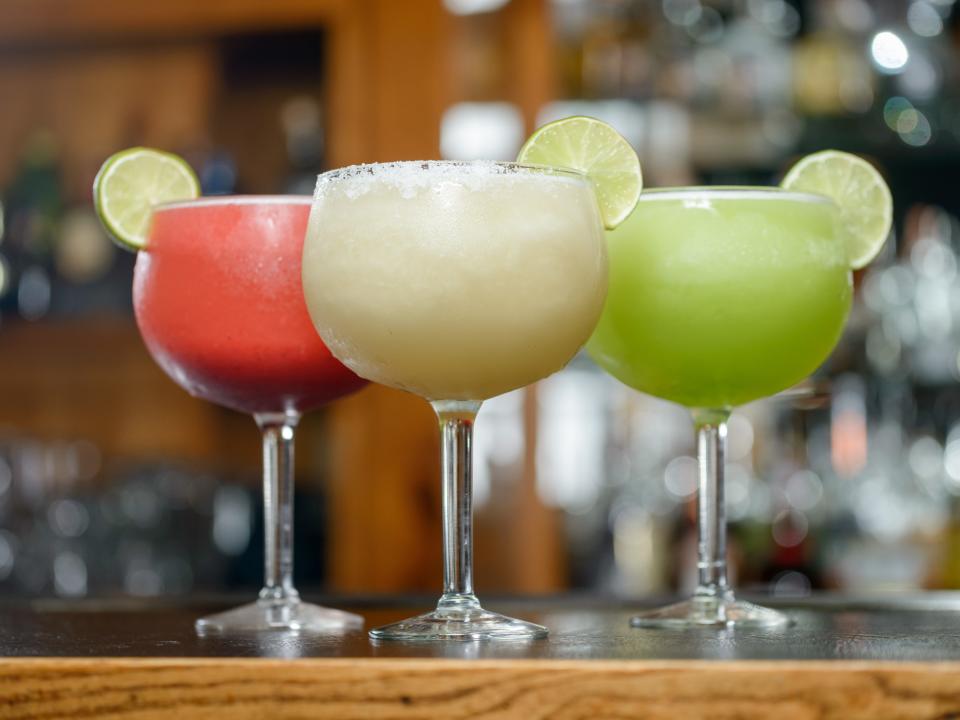a trio of frozen margaritas (red, white, and green) lined up on a bar