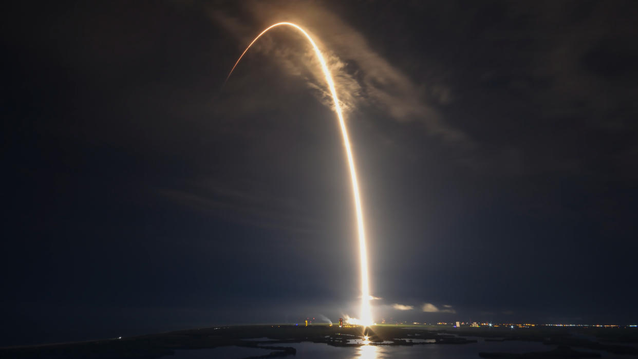  a spacex falcon 9 rocket makes a yellow-orange arc in a dark sky during launch 