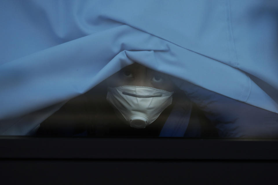 A passenger who disembarked from the quarantined Diamond Princess cruise ship peeks out of a bus window, Feb. 19, 2020, in Yokohama, near Tokyo. (AP Photo/Jae C. Hong)