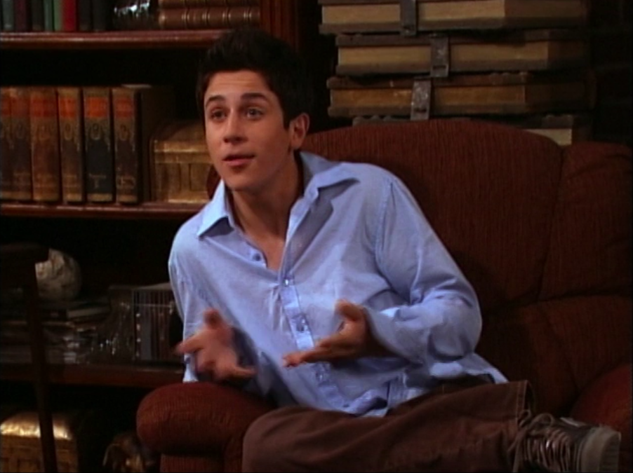 David Henrie as Justin Russo sits on a chair in a button down shirt