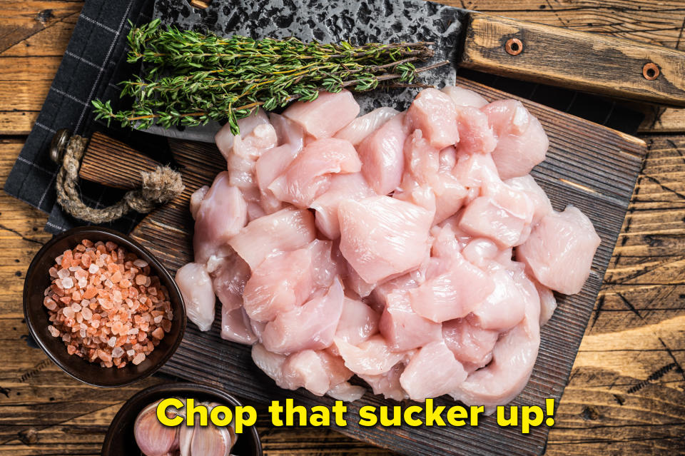 A raw chicken breast cut into cubes on a wooden board