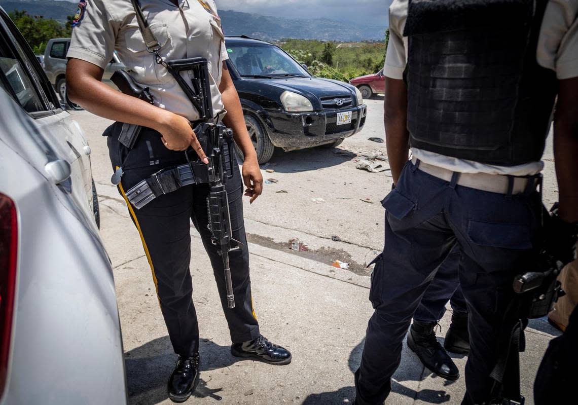 A heavily armed Haitian policewoman on June 23, 2022, keeps watch as Tabarre Police Commissioner Livenston Gauthier (not pictured) talks to two rookie police officers at a checkpoint near the U.S. Embassy on the outskirts of Port-au-Prince.