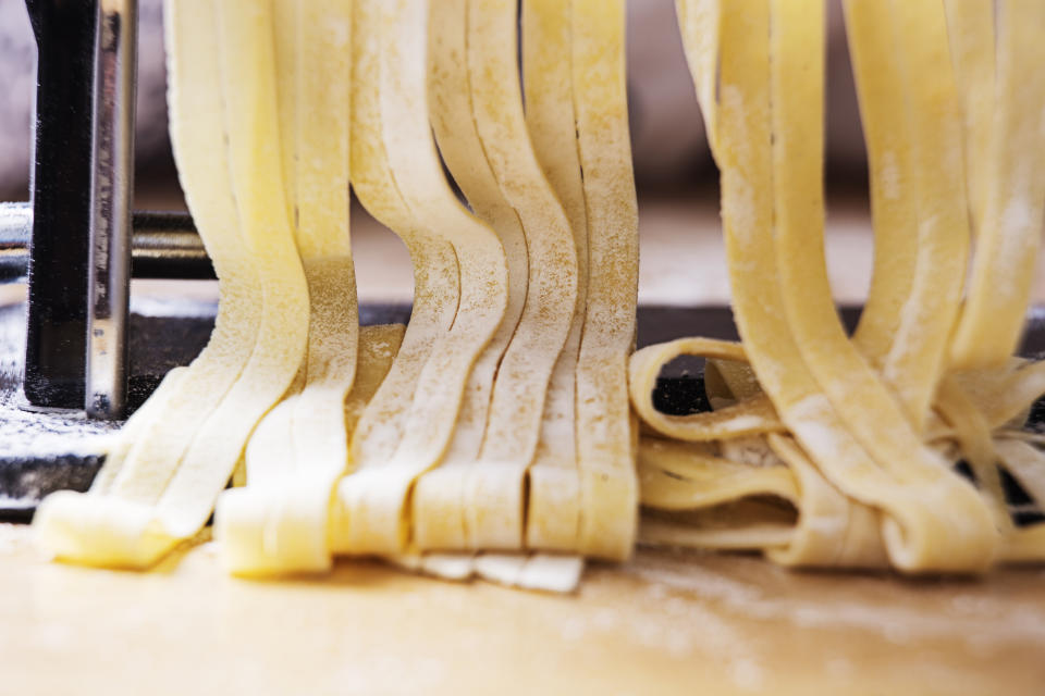 Fresh pasta dough being cut into noodles by a pasta machine