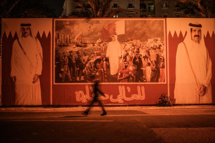 A person walks past a board showing the Emir of Qatar and his father (Quentin Muller)