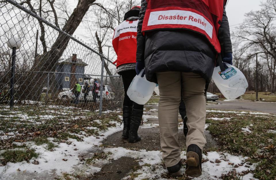 Members of the Red Cross carry jugs of purified water while going door-to-door delivering the free purified jugs of water and water filters to Flint residents dealing with the water crisis on the the city's north side on Friday Jan. 8, 2016, while helping the members of the Genesee County Sheriff's Department and the Sheriff's Reserve.