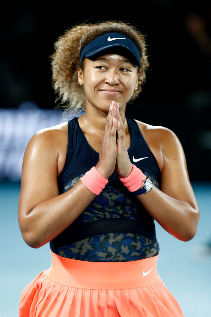 Naomi holds her hands together in front of her face as she acknowledges the crowd from the tennis court