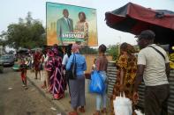 People stand in line under a campaign billboard showing the candidats of the ruling coalition party, the Rally of Houphouetists for Democracy and Peace (RHDP) ahead of the legislative election in Abidjan