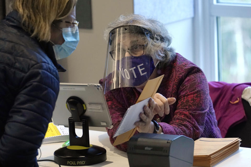 Poll worker Alice Machinist, of Newton, Mass., right, wears a mask and shield out of concern for the coronavirus while assisting a voter, left, with a ballot during early in-person general election voting, Wednesday, Oct. 28, 2020, at the Newton Free Library, in Newton, Mass. (AP Photo/Steven Senne)