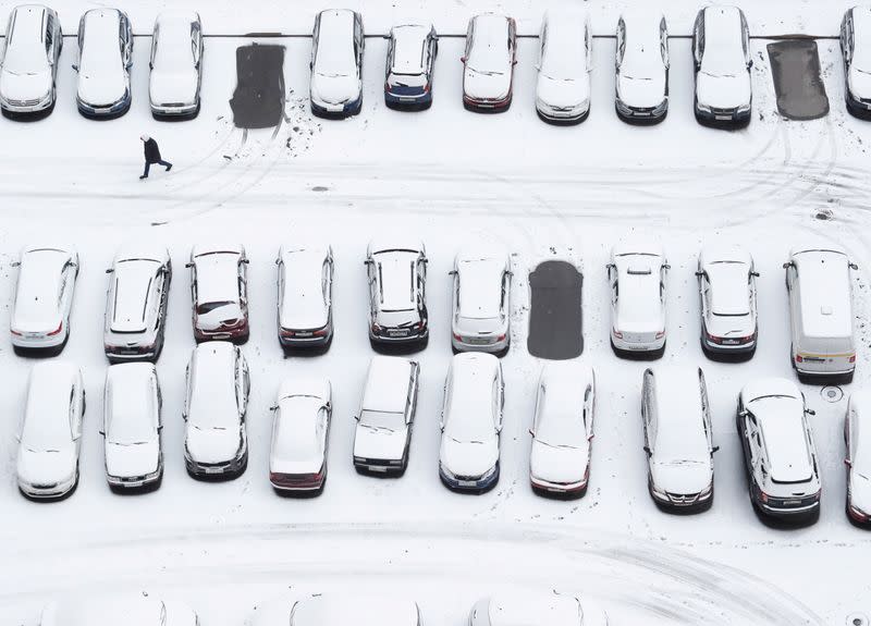 A person walks past cars covered with snow in the parking lot in Saint Petersburg