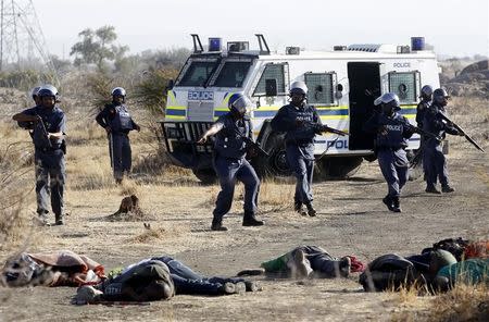 ATTENTION EDITORS - VISUAL COVERAGE OF SCENES OF DEATH AND INJURY A policeman gestures in front of some of the dead miners after they were shot outside a South African mine in Rustenburg, 100 km (62 miles) northwest of Johannesburg, August 16, 2012. South African police opened fire on Thursday against thousands of striking miners armed with machetes and sticks at Lonmin's Marikana platinum mine, leaving several bloodied corpses lying on the ground. A Reuters cameraman said he saw at least seven bodies after the shooting, which occurred when police laying out barricades of barbed wire were outflanked by some of an estimated 3,000 miners massed on a rocky outcrop near the mine, 100 km (60 miles) northwest of Johannesburg. REUTERS/Siphiwe Sibeko (SOUTH AFRICA - Tags: CIVIL UNREST CRIME LAW TPX IMAGES OF THE DAY) TEMPLATE OUT