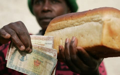 A woman holds a loaf of white bread and costing 45,000 Zimbabwean dollars in 2006 - Credit: Howard Burditt/REUTERS