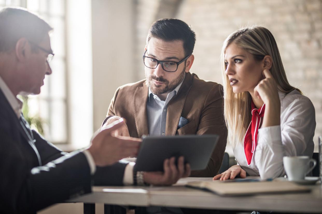 young couple and their real estate agent looking at housing plan on touchpad in the office