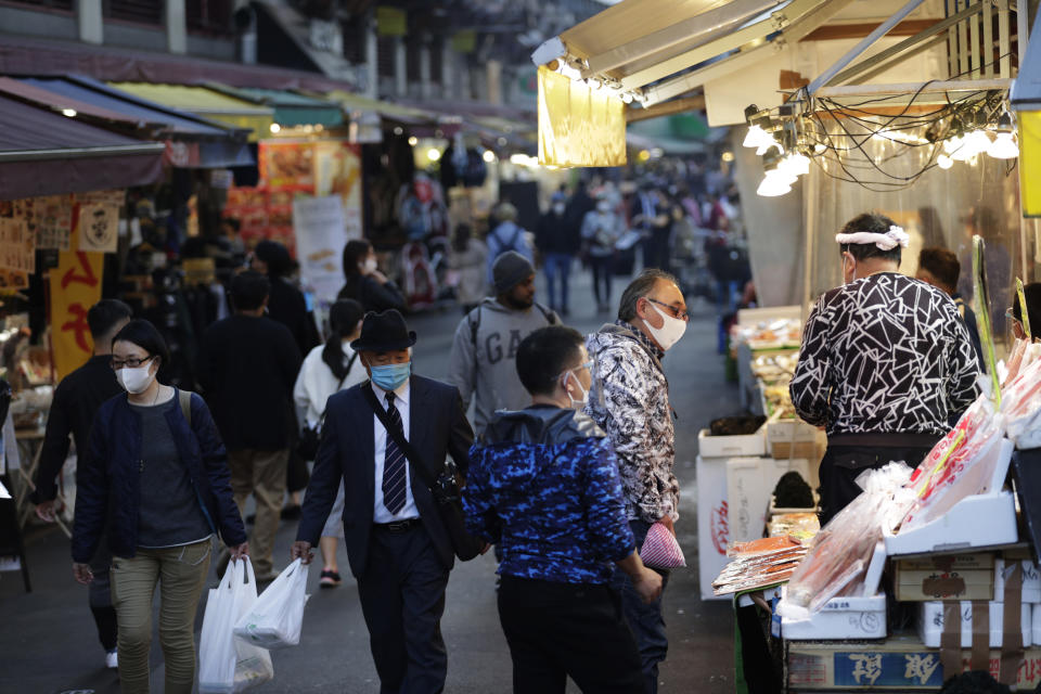 A shopper, second right, wearing a face mask buys sea food at a shopping street in Tokyo on Thursday, Nov. 19, 2020. Japan's number of reported coronavirus infections hit a record high Thursday, and the prime minister urged maximum caution but stopped short of calling for restrictions on travel or business. (AP Photo/Hiro Komae)