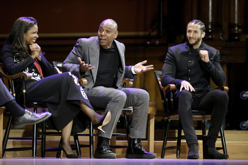 FILE - In this Oct. 11, 2018, file photo, comedian Dave Chappelle, center, shares a light moment with philanthropist Pamela Joyner, left, and former NFL quarterback Colin Kaepernick, right, on stage during W.E.B. Du Bois Medal award ceremonies at Harvard University in Cambridge, Mass. When George Floyd died under the knee of a Minneapolis policeman, Harvard basketball coach Tommy Amaker knew it was time to get to work. Amaker brings players to the annual W.E.B. Du Bois Award ceremony, where Harvard honors trailblazers in politics, culture and business. Among them are Chappelle and Kaepernick. (AP Photo/Steven Senne, File)