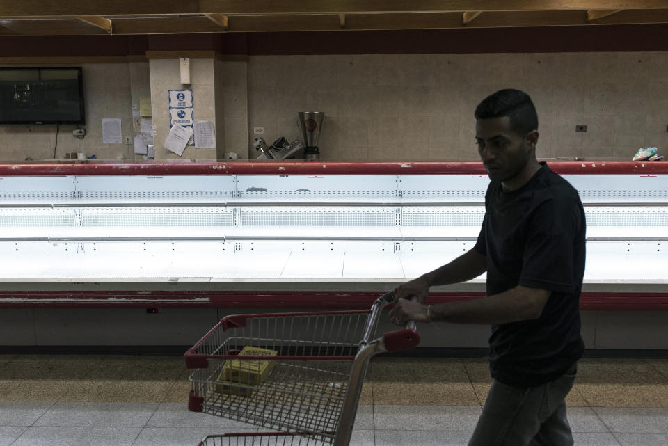 A customer pushes a shopping cart past an empty meat counter at a grocery store in Caracas, Venezuela, on Jan. 9, 2018. Hordes of desperate shoppers emptied supermarkets and bodegas after the government ordered hundreds of grocery stores slash their prices in the latest attempt to stem hyperinflation.