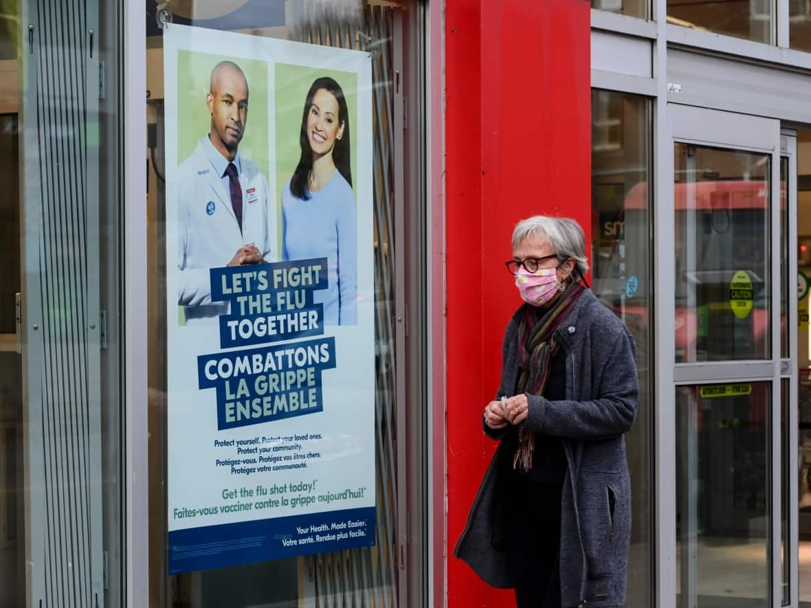 A woman walks past a flu shot sign on a pharmacy on Oct. 15, 2020. The B.C. Ministry of Health says flu shots will be free in the province for everybody except infants younger than six months old. (Sean Kilpatrick/Canadian Press - image credit)