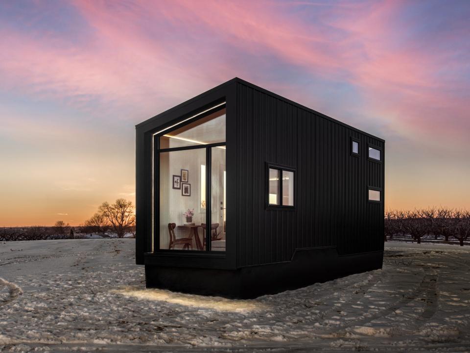 a black tiny home with a large glass wall on a snowy field