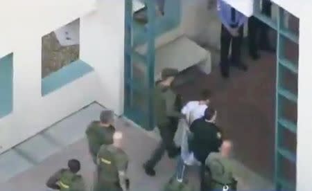 Police escort a suspect into the Broward Jail after checking him at the hospital following a shooting incident at Marjory Stoneman Douglas High School in Parkland, Florida, U.S. February 14, 2018 in a still image taken from a video. WSVN.com via REUTERS