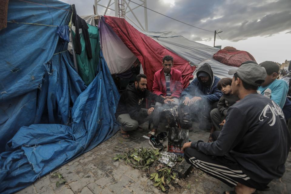 Displaced Palestinians sit by a lit fire in front of their tent and inspect the damage caused by rain on Wednesday in Khan Yunis, Gaza. Heavy fighting rages in the northern Gaza Strip as Israel encircles the area despite increasingly pressing calls for a cease-fire.