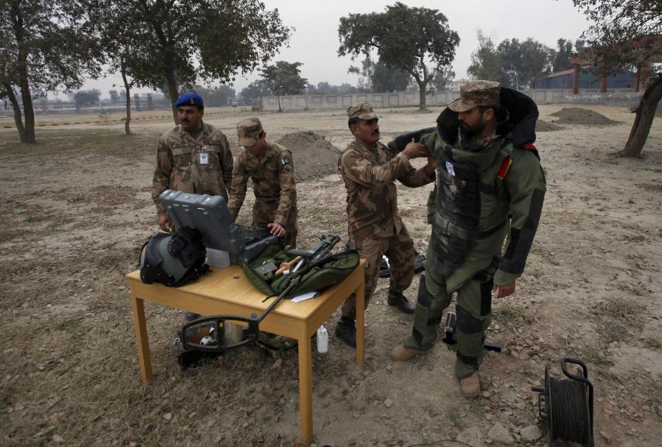 In this Wednesday, Jan. 8, 2014, photo, A Pakistani soldier helps his colleague to put on a bomb suit for a training session at the Counter IED Explosives and Munitions School, in Risalpur, Pakistan. Militants in Pakistan have become devilishly ingenious about where they plant improvised explosive devices, a type of bomb responsible for thousands of wounds and deaths in Pakistan. They’ve been found strapped to children’s bicycles, hidden inside water jugs and even hung in tree branches. (AP Photo/Anjum Naveed)