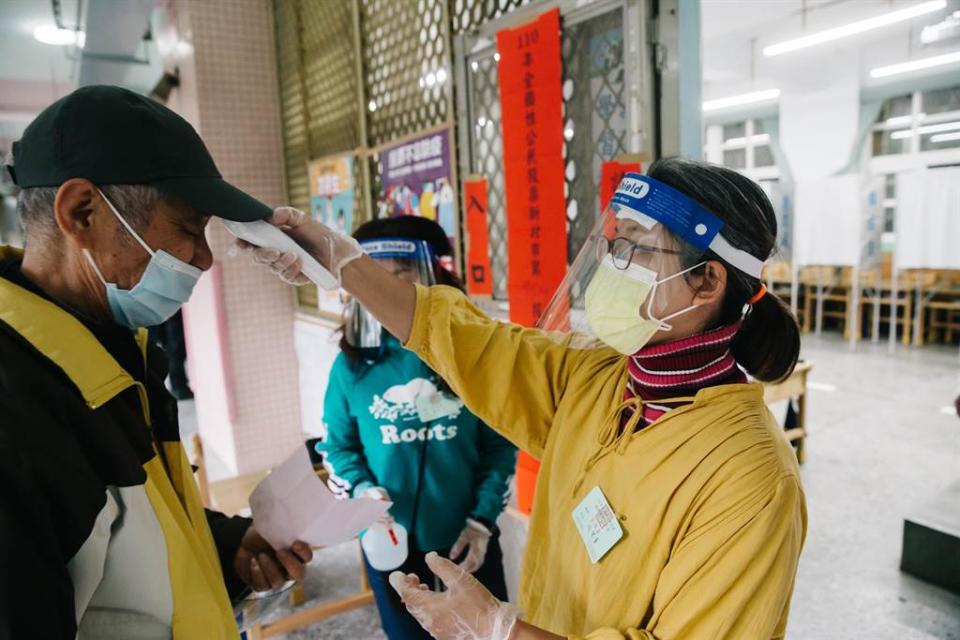 四大公投案18日登場，投票站入口有選務人員頭戴防護面罩、攜帶酒精、體溫計確保符合防疫規範；選務人員為民眾量體溫。(郭吉銓攝)