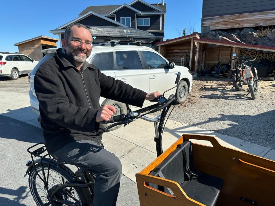 Andrew Robinson, a renewable energy consultant, on his electric cargo bike in Yellowknife on April 26, 2024. A plug-in hybrid vehicle and two other electric bikes are parked in the background.
