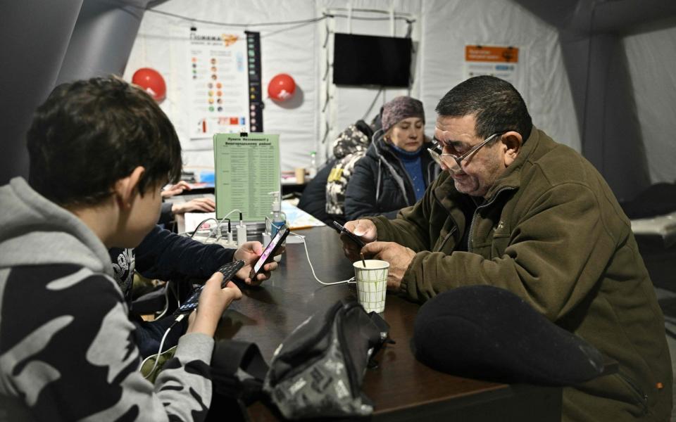 People charge their devices, use internet connection and warm up inside a Point of Invincibility a mobile heating point set in the town of Vyshgorod, outside of Kyiv - GENYA SAVILOV/AFP via Getty Images