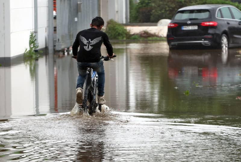 A cyclist rides across a flooded road. Karl-Josef Hildenbrand/dpa